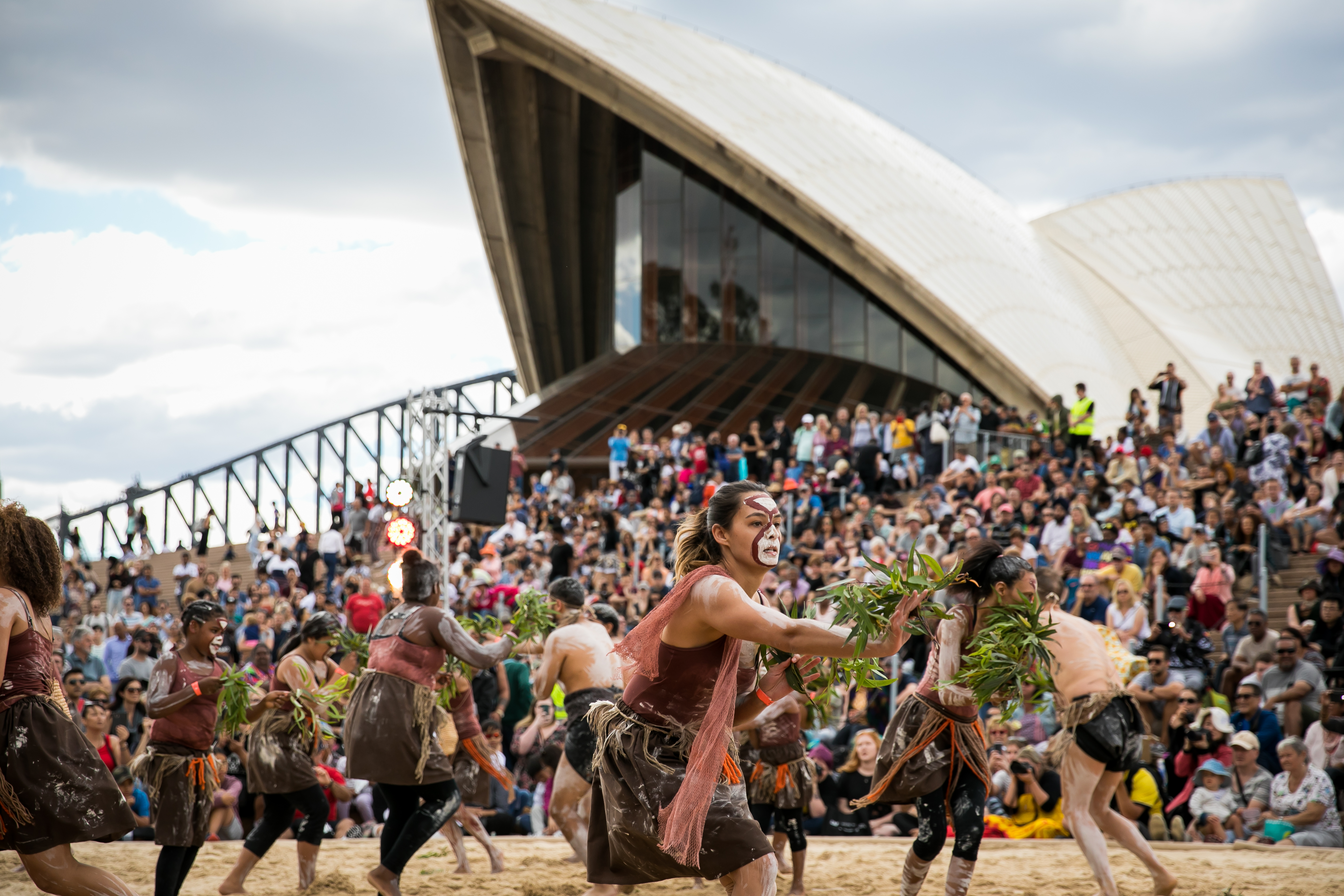 Women in sand pit performing indigenous dance in the Homeground of Sydney opera house.