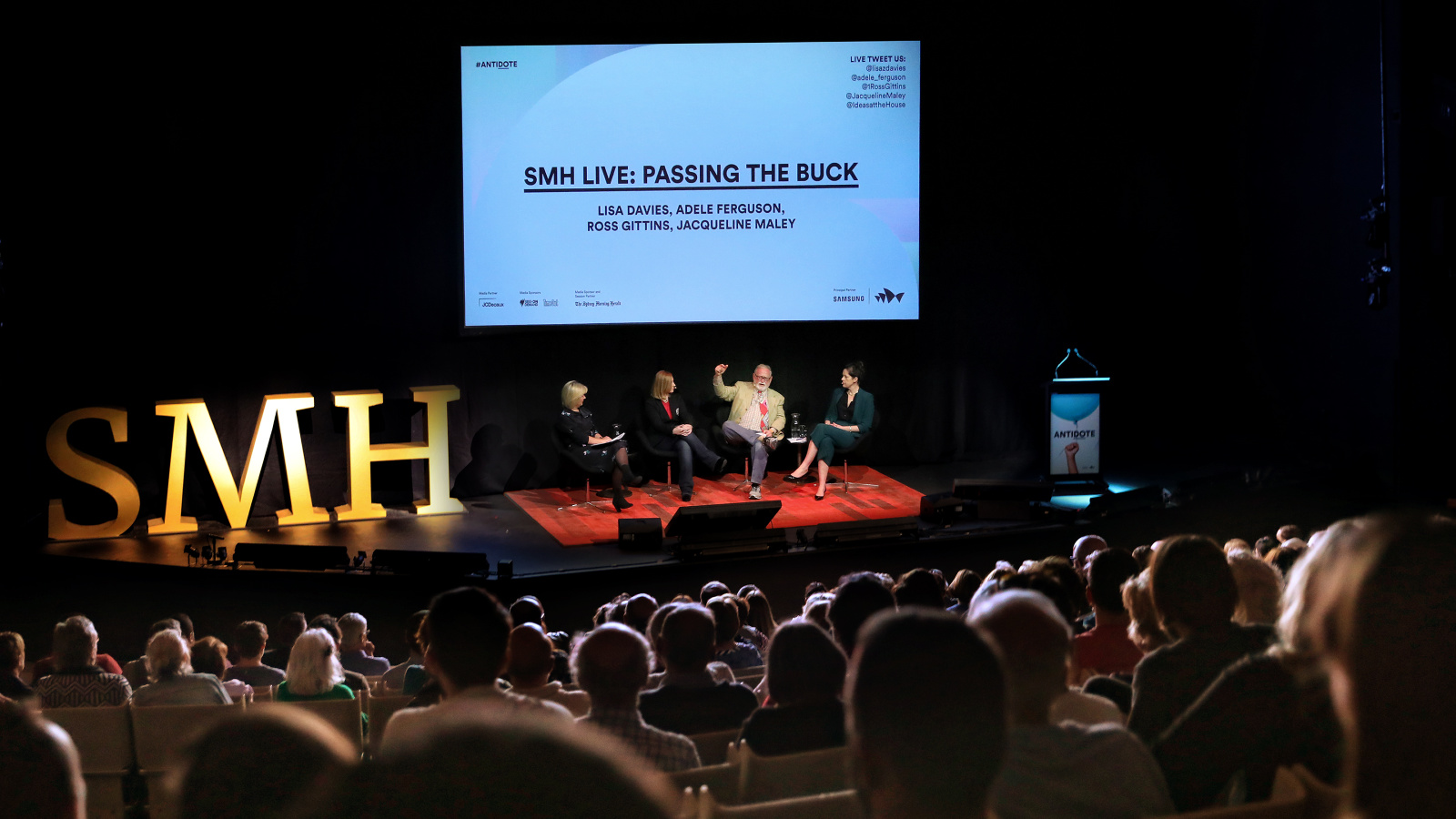 A seated audience watching four people on stage doing a presentation.