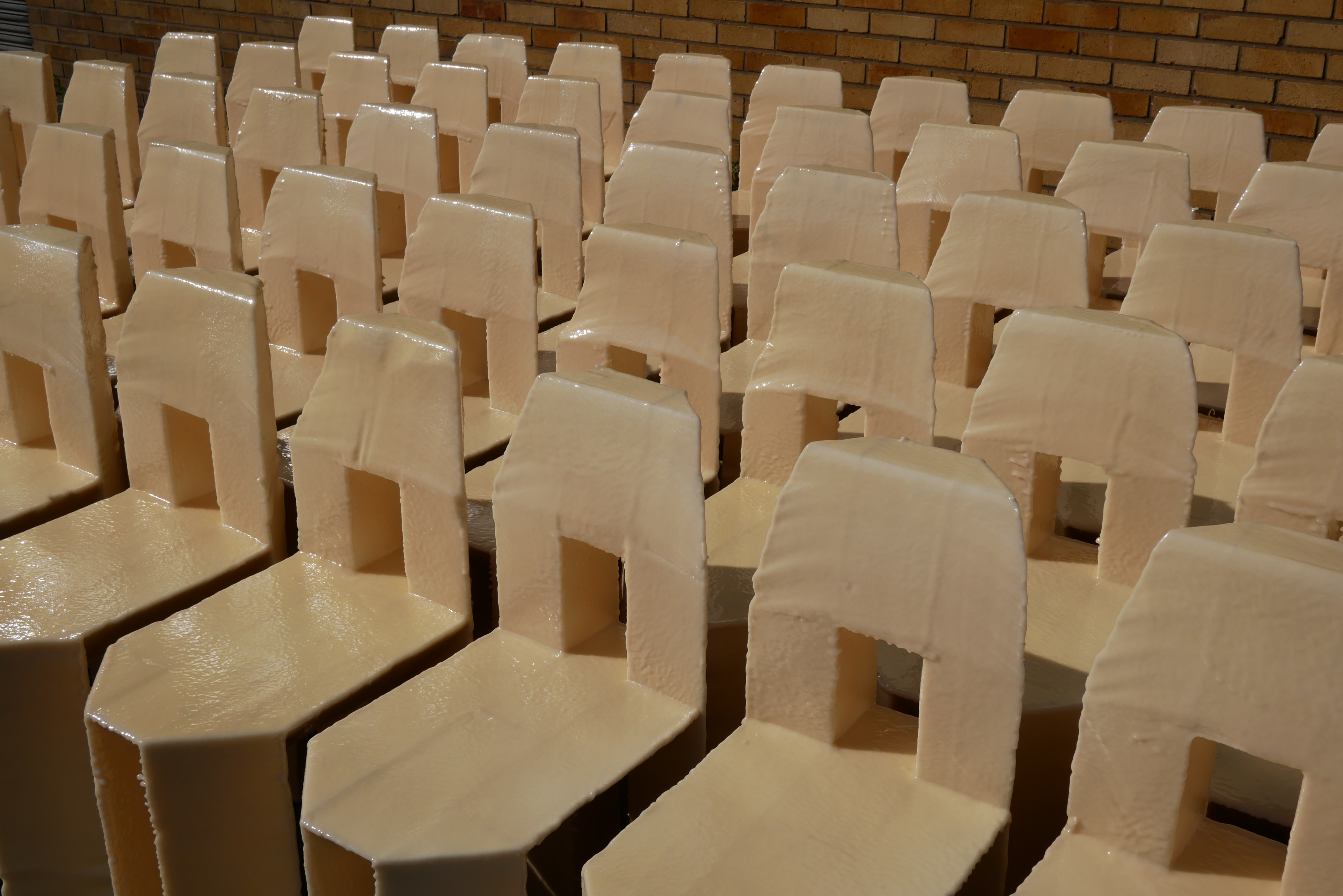 A group of 20 cream chairs with a square cut out in the back sit angled to the left in the sun.