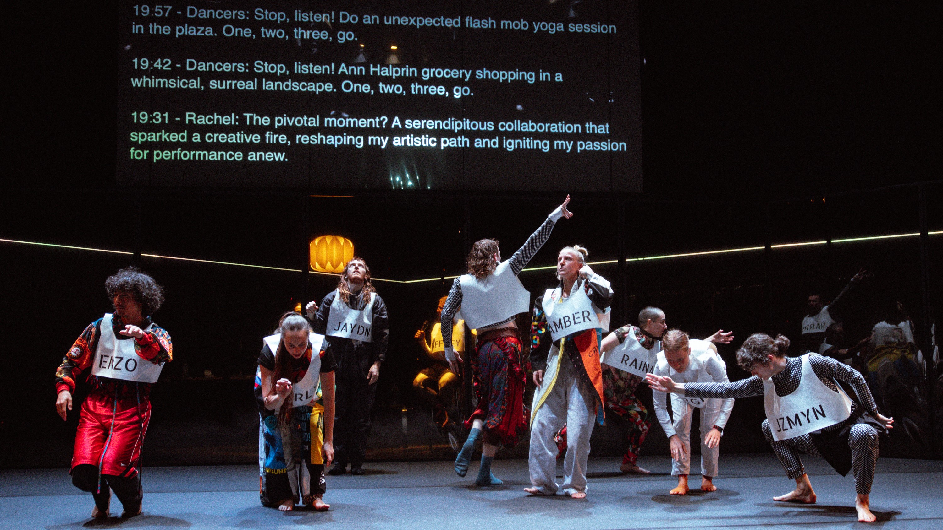 A diverse group of individuals stands on stage, dancing in front of a large projector screen displaying AI-generated text as movement suggestions.