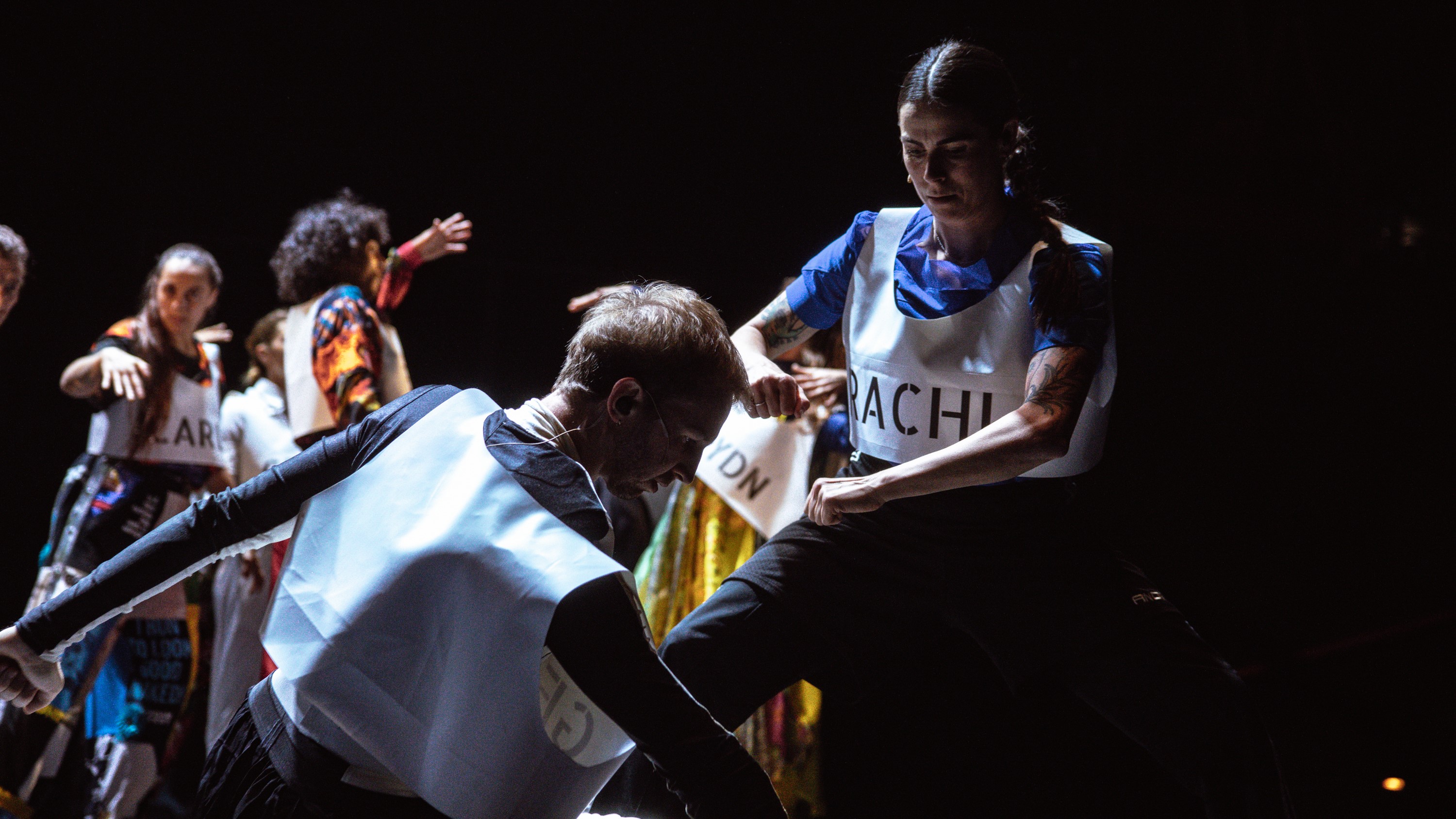 A male kneeling and female dancer standing face each other mid-movement.