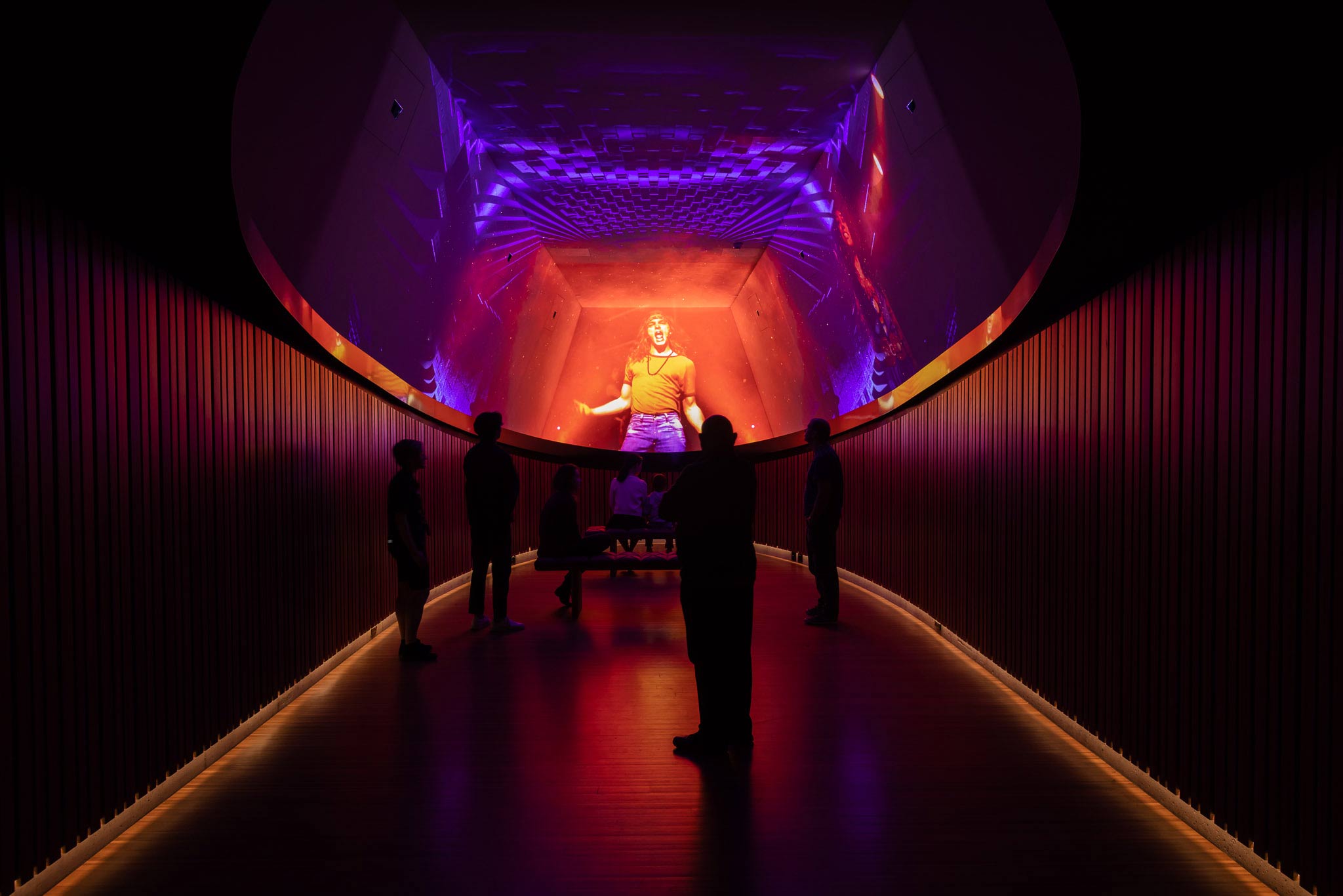 A group of visitors watching a projection of an event on ceiling screens.