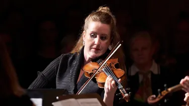 A female violinist plays the violin in front of a Chamber Orchestra