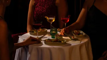 A round table with a white table cloth filled with canapes and cocktails for the VIP Gatsby at The Green Light experience, with moody, candle lit lighting.