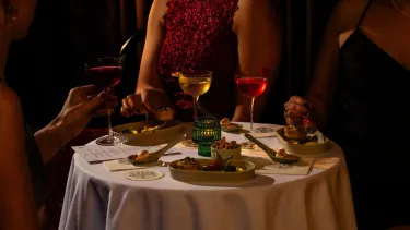 A round table with a white table cloth filled with canapes and cocktails for the VIP Gatsby at The Green Light experience, with moody, candle lit lighting.