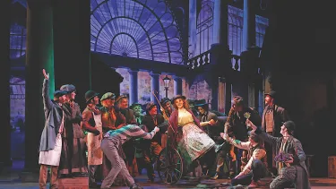 Eliza Doolittle with a cane surrounded by the company.