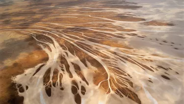 A very wide bird's eye view of empty brown arid land with river systems zip zagging through the land