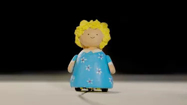 A small doll with blonde hair smiles. She wears a blue dress.