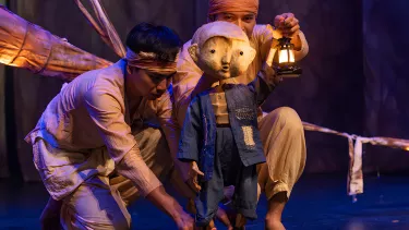 Two men hold a beautifully crafted puppet of a young child holding a lantern.