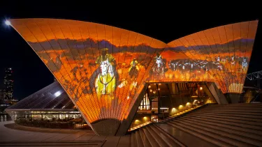 The Sydney Opera House sails at night, illuminated with an Australian outback landscape in orange and browns.