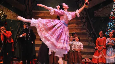 A ballet dancer in a pink dress leaping whilst holding a nutcraker.