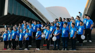 A group of people wearing blue stand on the steps of the Sydney Opera House.