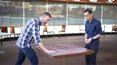 Two men standing looking over a table.