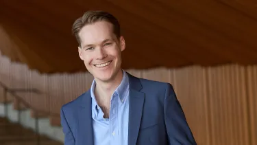 Harry Prouse wearing a blue suit, standing inside the Sydney Opera House.