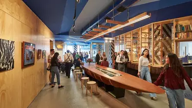 People walking through a room with a long table with hung artwork on the walls.