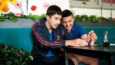 Two boys seated at a table, looking at their wire creation.