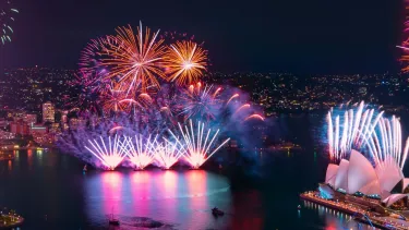 Sydney Harbour at night with fireworks over the Sydney Opera House and Sydney Harbour Bridge.