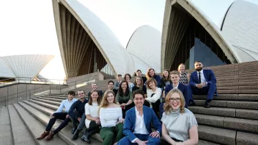 A group of men and women sitting on the staircase of Sydney opera house.