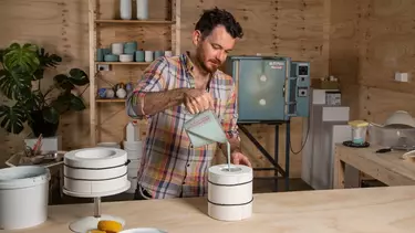 A man in a shirt pouring liquid into a rounded object.