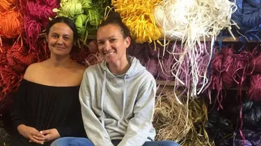 Two women seated, smiling in front of colorful materials.