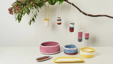 Five knitted buckets hanging off a branch underneath three colored bowls.