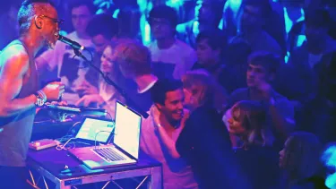 A DJ performing on stage to a lively audience.