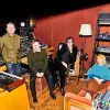 Three men and one woman in their 60s sit in a music recording studio.