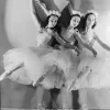Three ballerinas dancing together in white dresses.