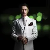 A man in a light grey suit and tie standing in front of a dark background with green lights.