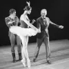 Two men in suits dancing with a ballerina in a white tutu.
