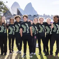 A group of people wearing black standing on the grass with the Sydney Opera House in the background.