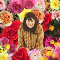 A lady with dark hair, a fringe and red lipstick infront of a floral background