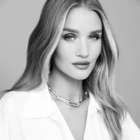 Black and white portrait of a woman with long hair, wearing a chain necklace and a white shirt. She gazes confidently at the camera.