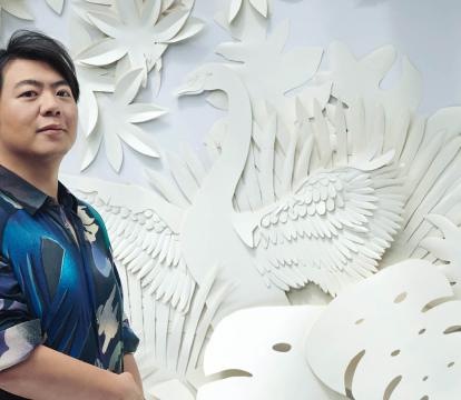 Pianist Lang Lang stands in front of a wall with an intricate cutout forest design