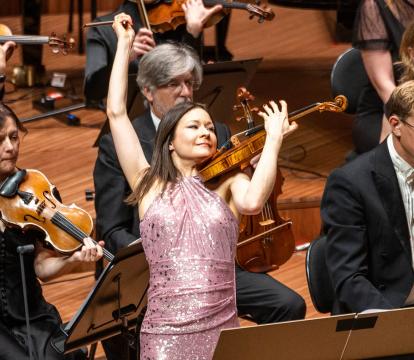 Violinist Arabella Steinbacher in a pink sequin dress flourishes the violin in front of the Sydney Symphony Orchestra violin section