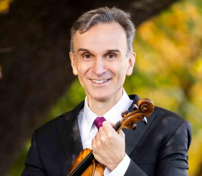 Gil Shaham holds a violin in a green forest.