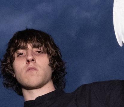 A white man with bowl-cut style hair looks down at the camera holding a white bird.