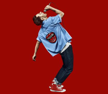 A man in a blue shirt stands confidently while holding a microphone, ready to speak or perform.