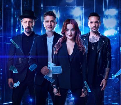 Four magicians face the camera, cards fall in front of them and they are lit by blue light.