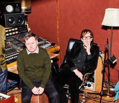 Three men and one woman in their 60s sit in a music recording studio.