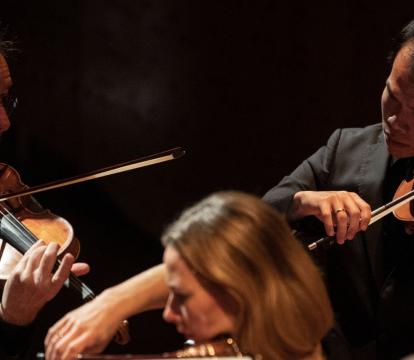 A 50-year old man plays violin next to another male violinist and a female violinist.