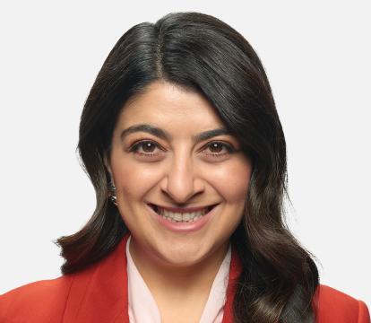 A smiling woman with dark brown hair, wearing a red blazer against a light grey background.