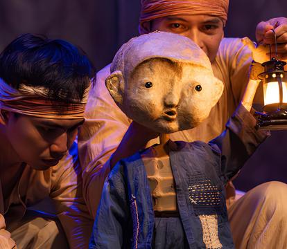 Two men hold a beautifully crafted puppet of a young child holding a lantern.