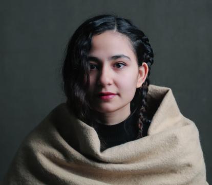 A young girl with dark hair wrapped in a beige blanket.