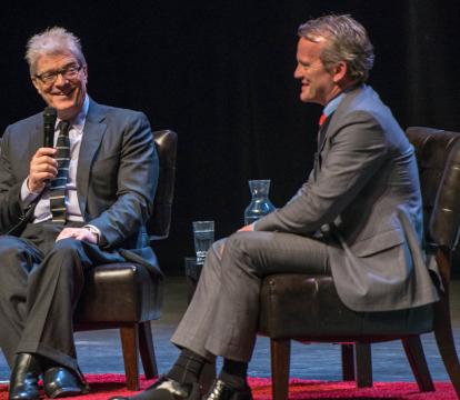 Two middle age men wearing suit, having a debate on the stage.