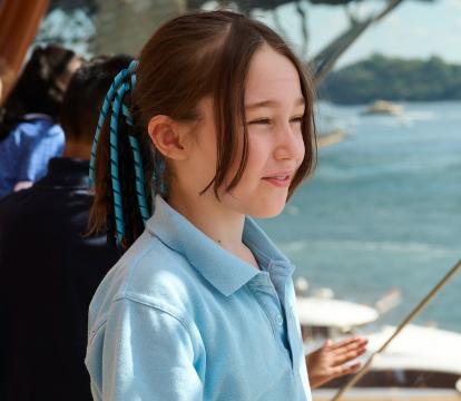 A young girl wearing a school uniform stares out a window in a Sydney Opera House foyer. The Sydney Harbour Bridge is seen in the background.