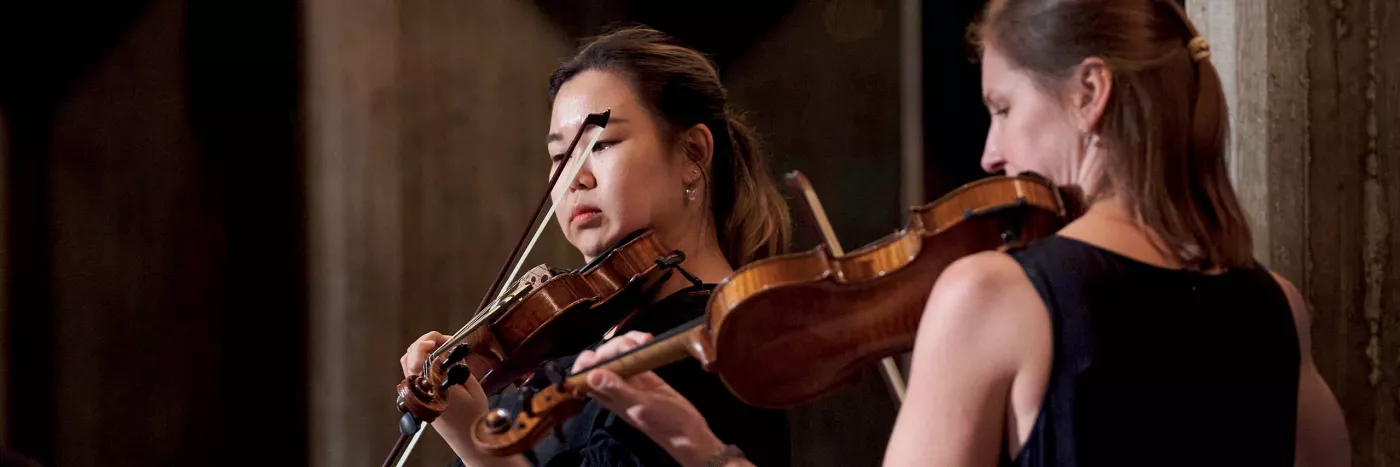 Two female violin players stand playing the violin