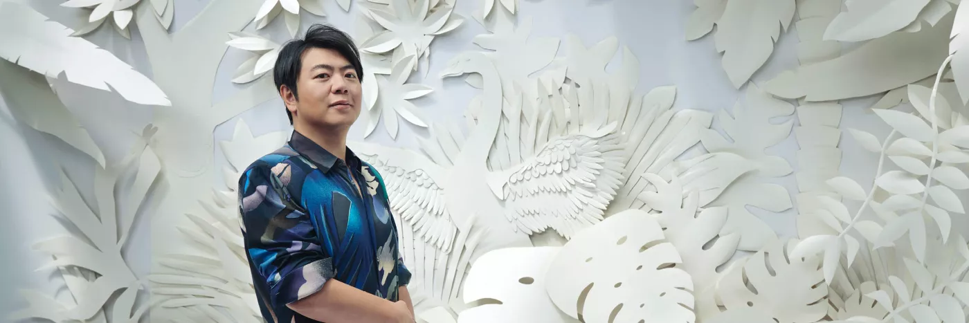 Pianist Lang Lang stands in front of a wall with an intricate cutout forest design