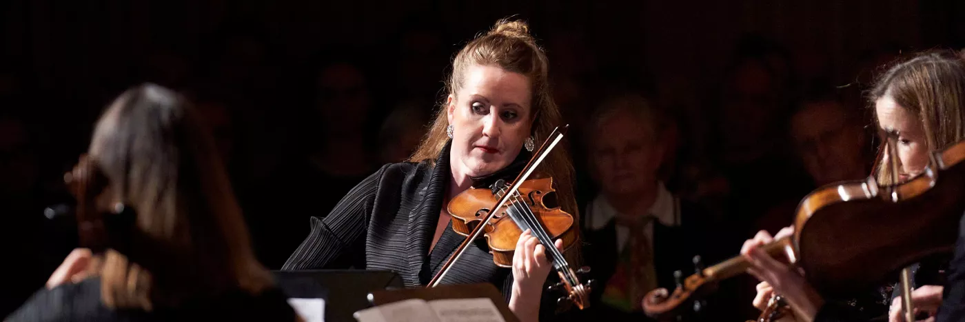 A female violinist plays the violin in front of a Chamber Orchestra