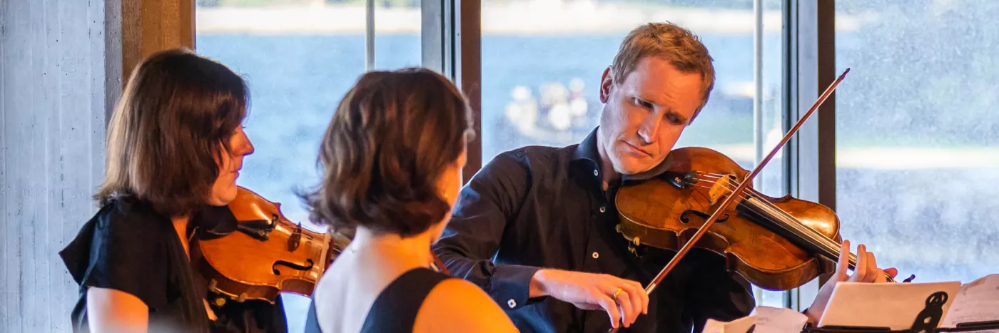 Three violin players stand playing the violin in the Sydney Opera House Utzon Room